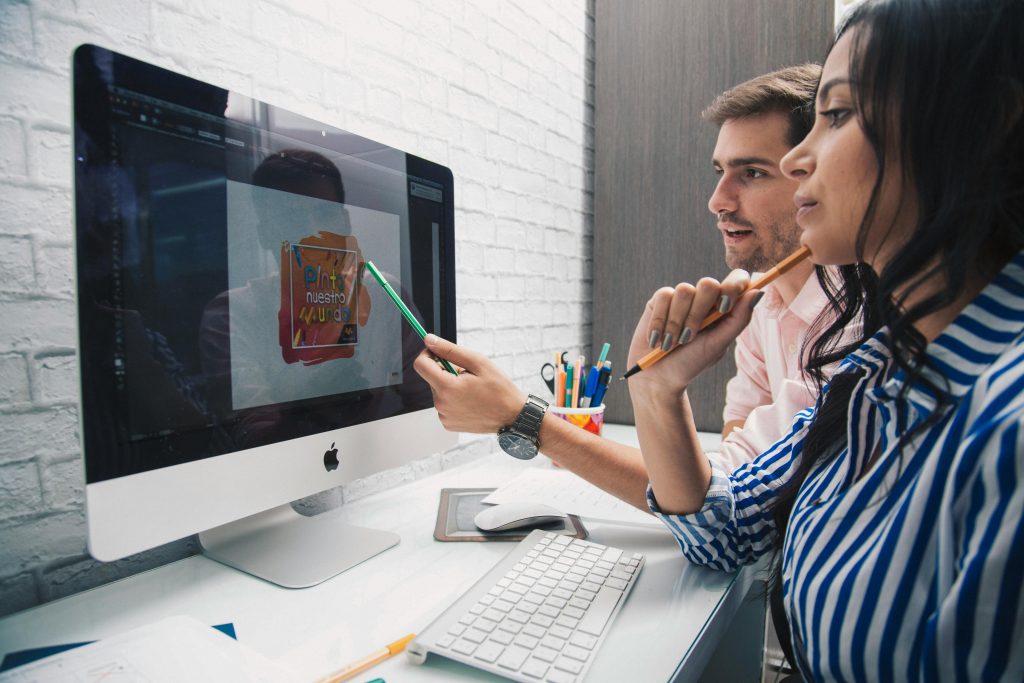 Side view of focused coworkers working together on graphic design while sitting at table and looking at monitor in modern office